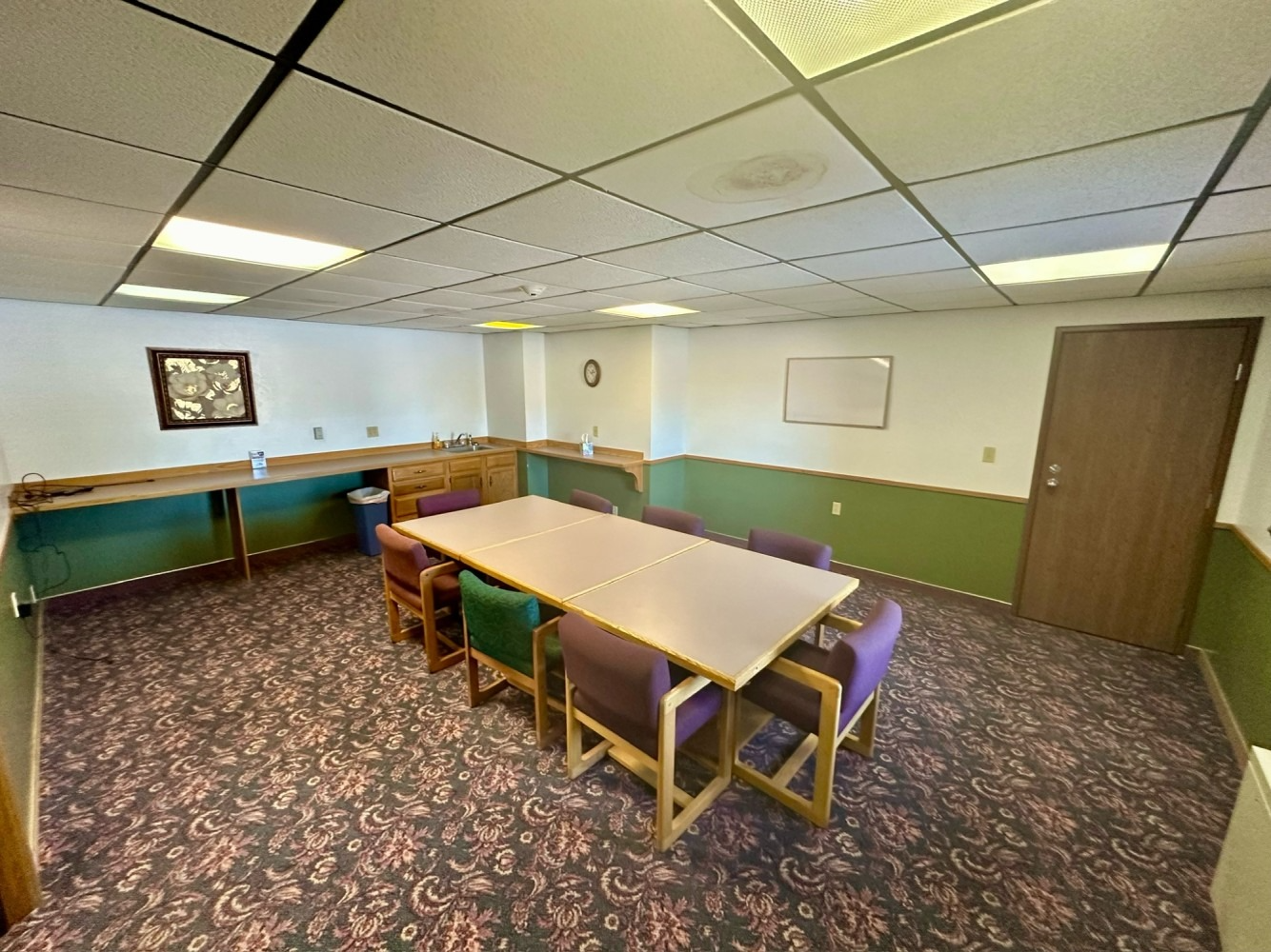Meeting room with long table, chairs, green and white walls, patterned carpet, and drop ceiling.