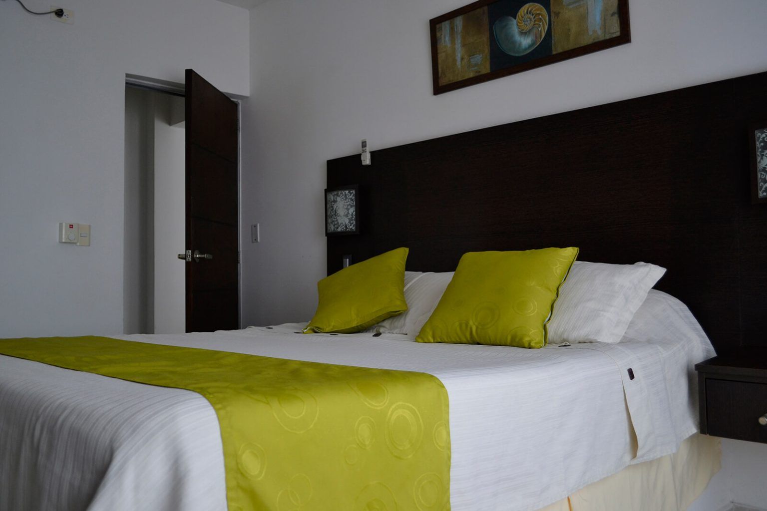Cama bien hecha con sábanas blancas, camino de mesa verde lima y almohadas en una habitación de hotel moderna.