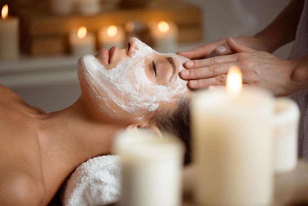 Person receiving a facial massage with cream in a candlelit spa room