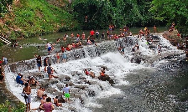 Gente nadando y sentada en una pequeña cascada en un río de bosque verde