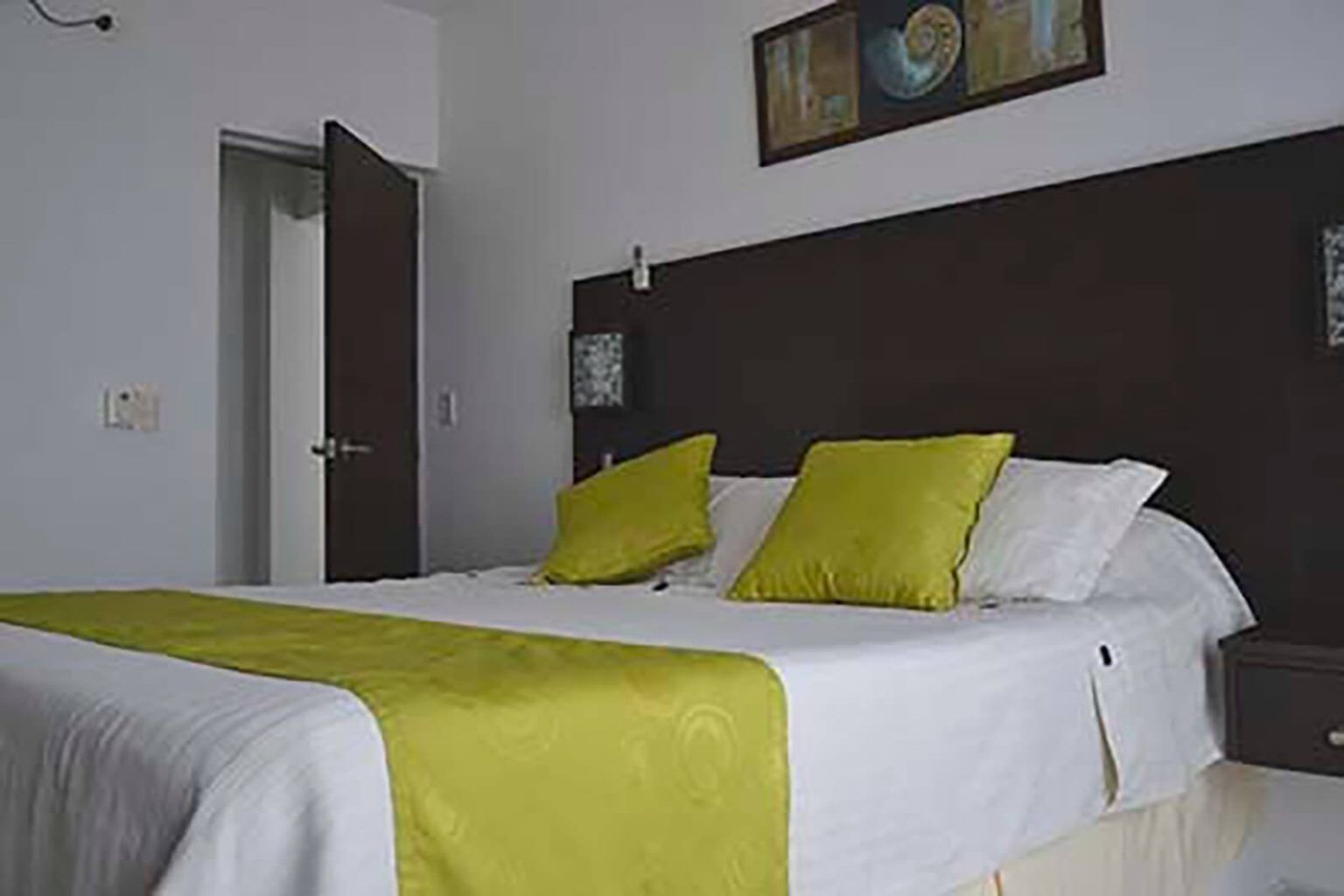 Dormitorio moderno con cabecero oscuro, ropa de cama blanca y almohadas y camino de mesa de color verde lima.