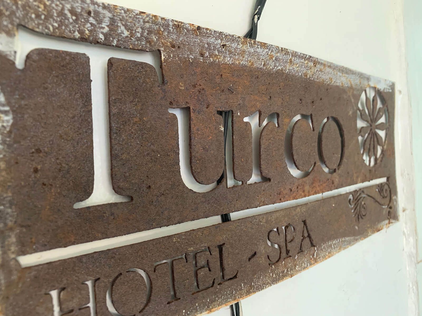 Letrero de metal desgastado con la inscripción “Turco Hotel Spa” en letras blancas sobre un fondo marrón oxidado.