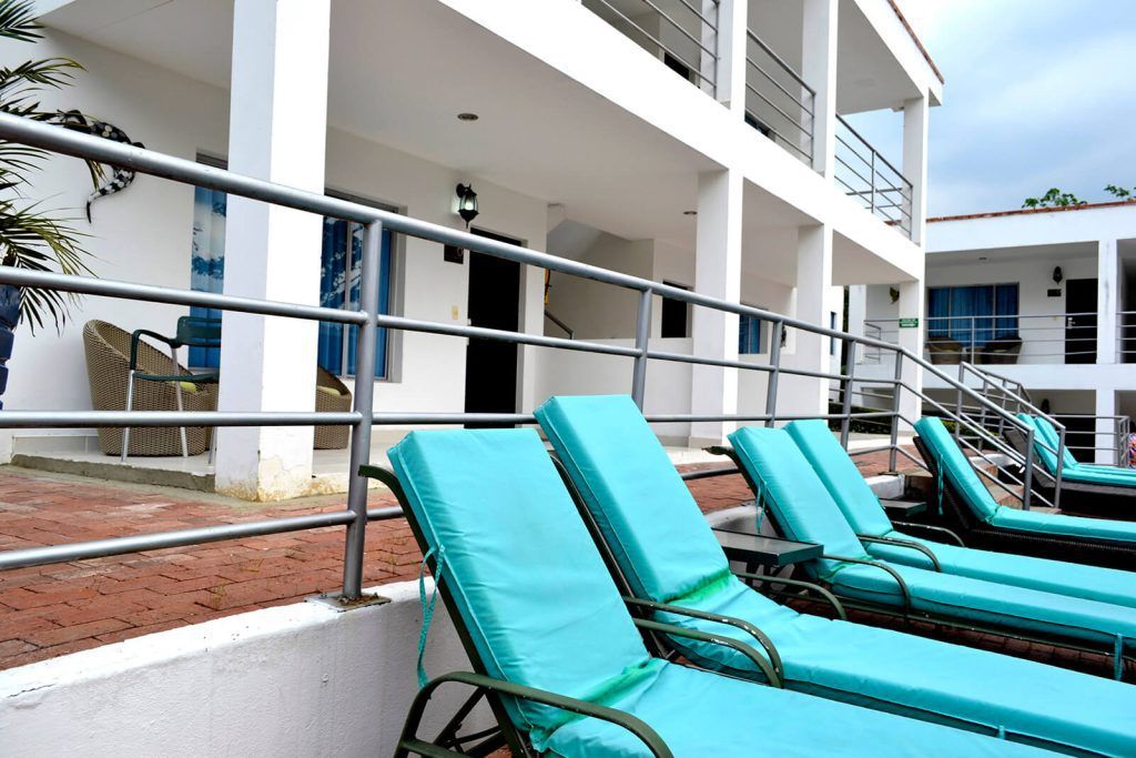 Tumbonas azules junto a un edificio blanco del complejo turístico con barandillas y balcones. Zona de piscina.
