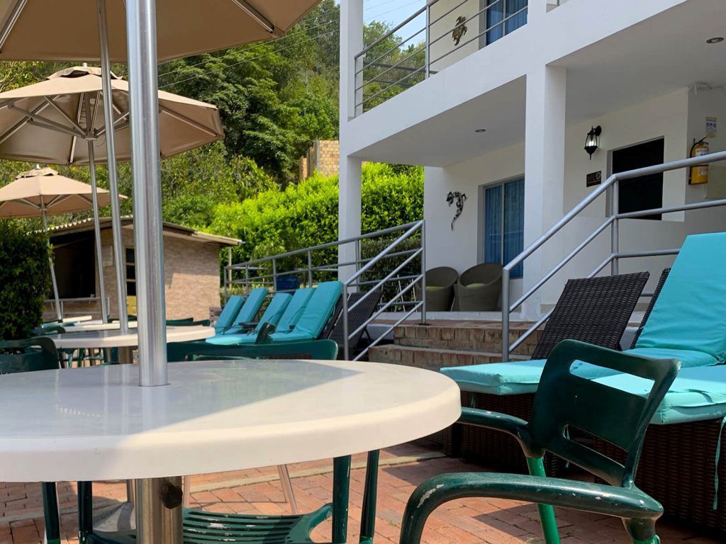 Patio con tumbonas turquesas, mesa blanca, sombrillas y una casa moderna al fondo.