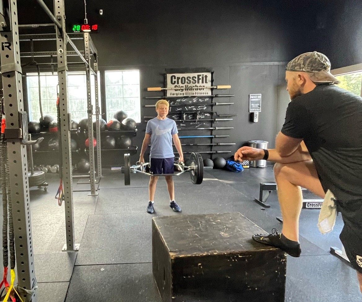 A man sitting on a box in a gym watching a man lift weights