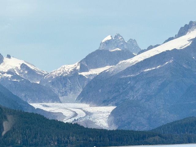 Glacier nestled between snow-capped mountains under a clear blue sky, seen from across a body of water.