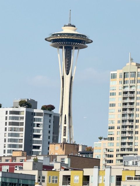 Space Needle with observation deck, Seattle, towers over surrounding buildings against a blue sky.