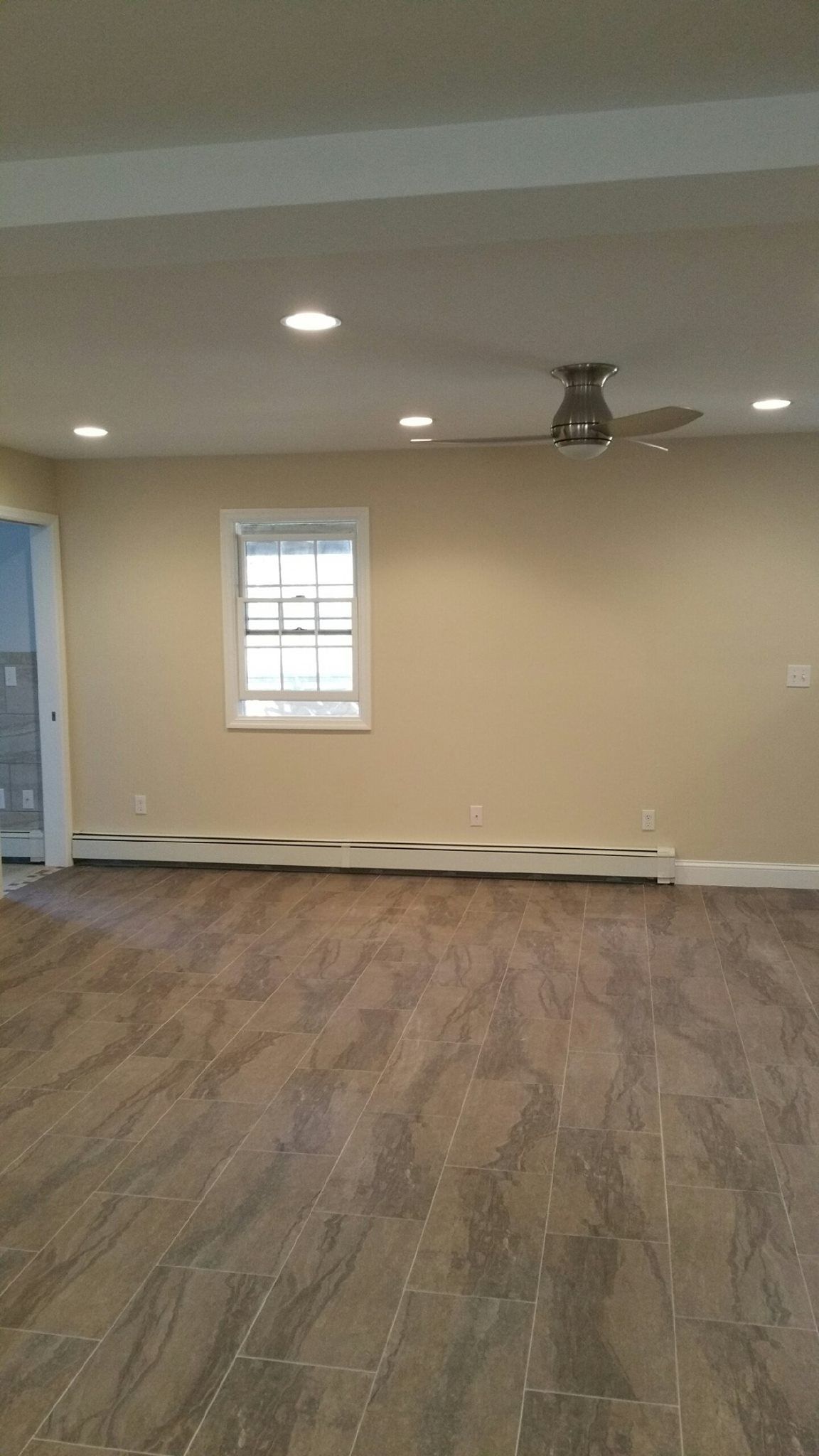 A large empty room with a ceiling fan and a window.