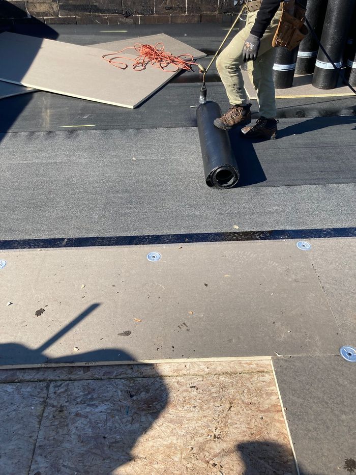 Person rolling out roofing material on a flat roof.