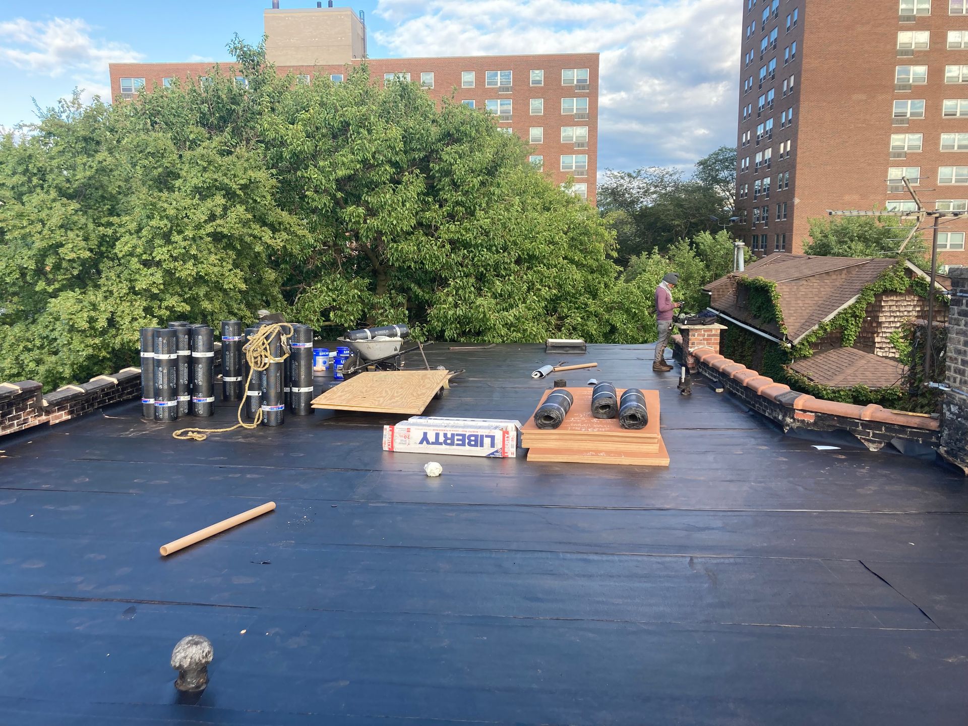 Rooftop scene with construction materials and trees. Buildings in the background. Blue sky.
