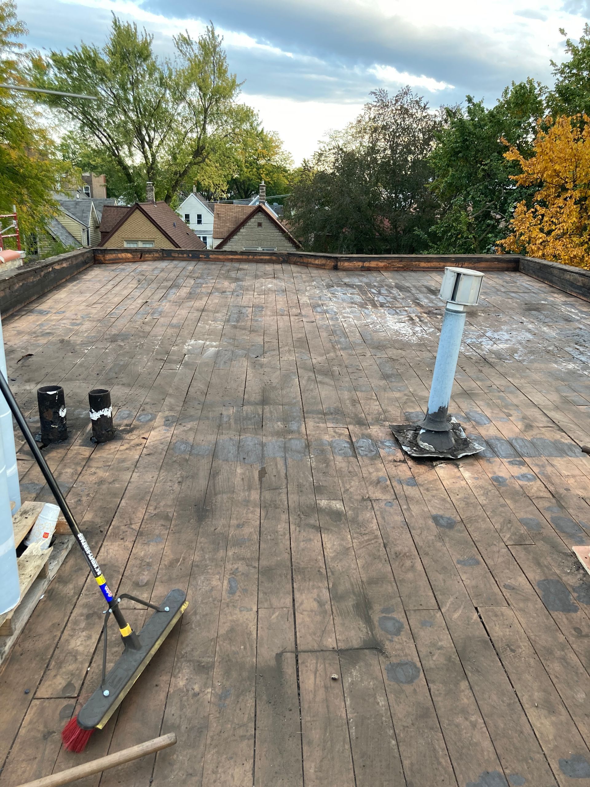 Flat rooftop with exposed wood, pipes, and a broom under a cloudy sky.