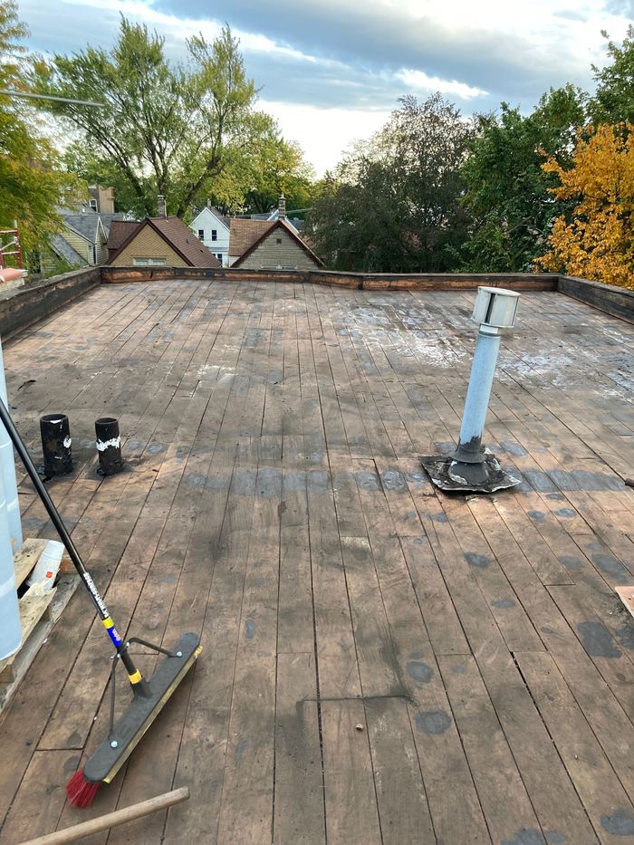 Flat roof with weathered wood, plumbing pipes, and a broom.