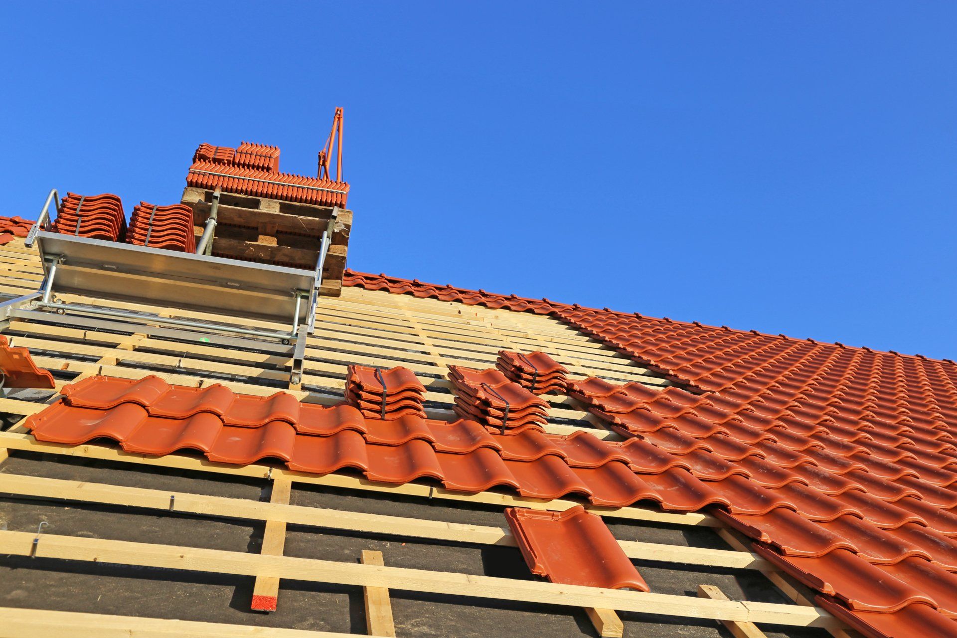 Roofing work in progress: red tiles being laid on a roof, blue sky backdrop.