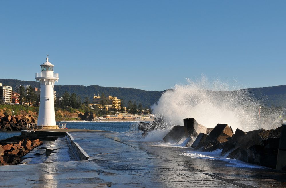 A Lighthouse On A Pier With Waves Crashing Against It — Sunblitz Window Tinting In Wollongong, NSW