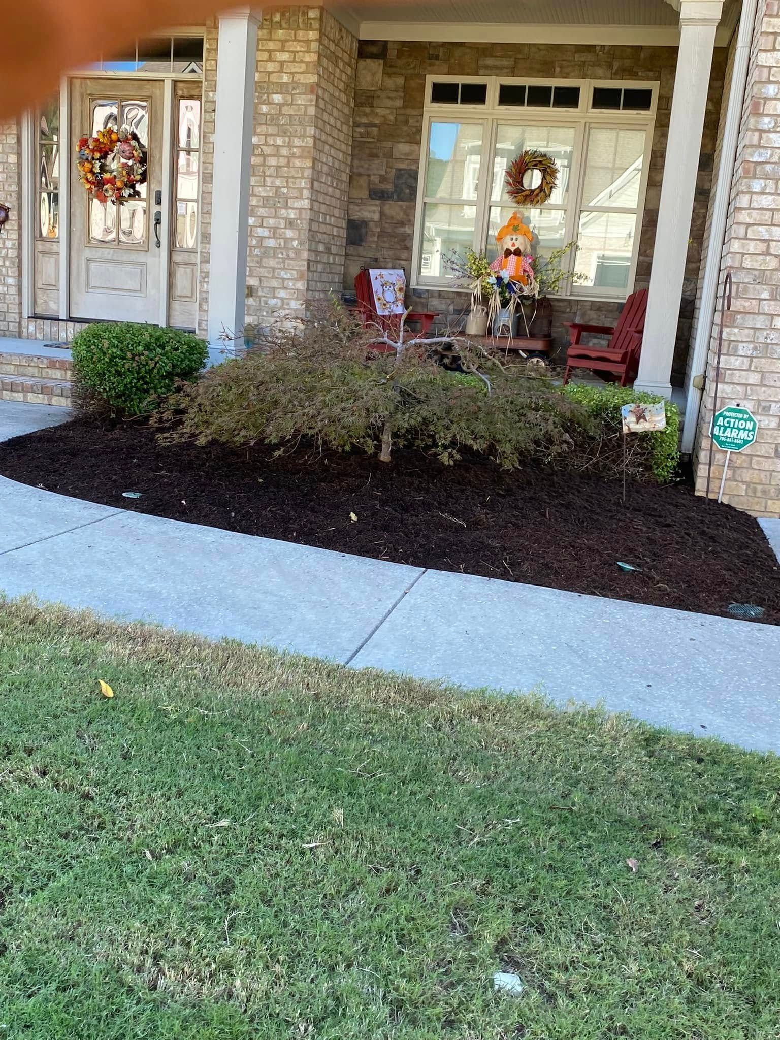 Front porch with wreaths, red chairs, and a landscaped front bed beside a lawn and sidewalk.