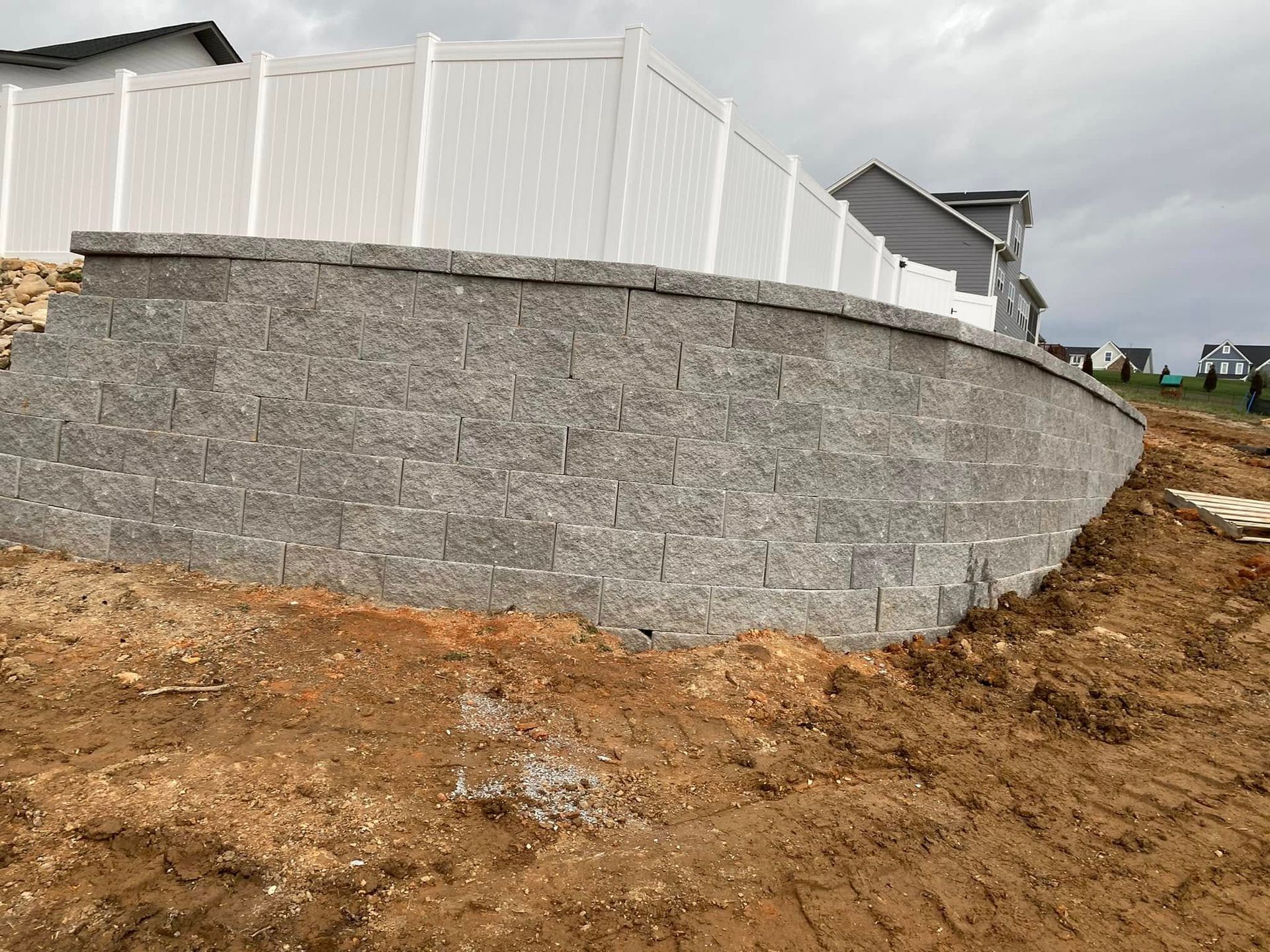 Curved gray stone retaining wall with white fence on a dirt slope at a construction site