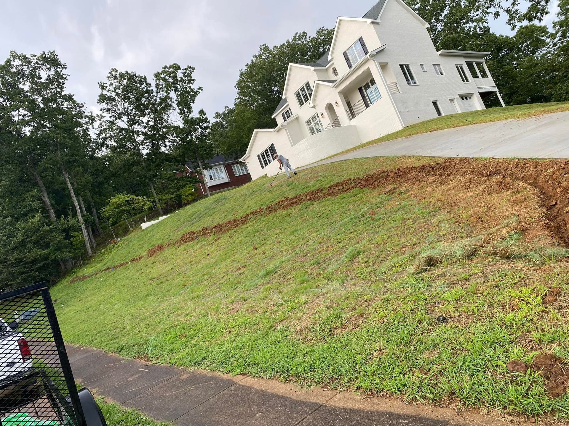 White house on a steep grassy hill beside a paved path and trees