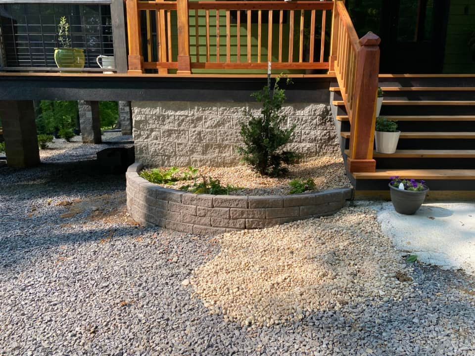 Backyard deck with wooden stairs, gravel path, raised stone planter, and small shrubs