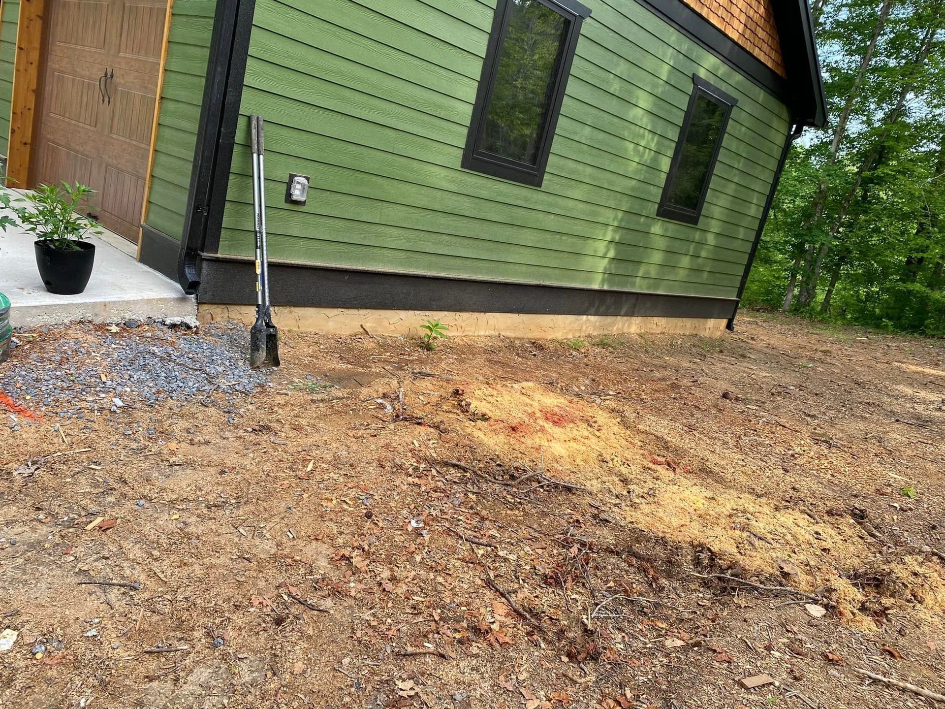 Yard work beside a house, with a person using a rake near a tree and a cleared dirt area.