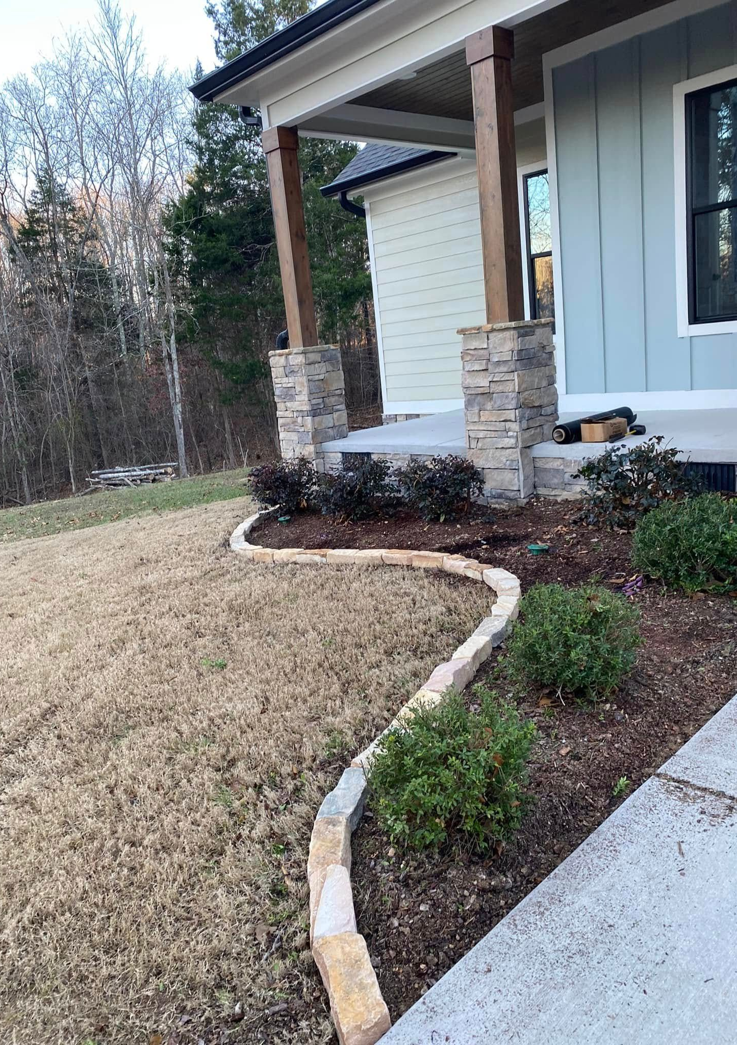 Front yard landscaping with curved stone edging, shrubs, and a covered porch on a house