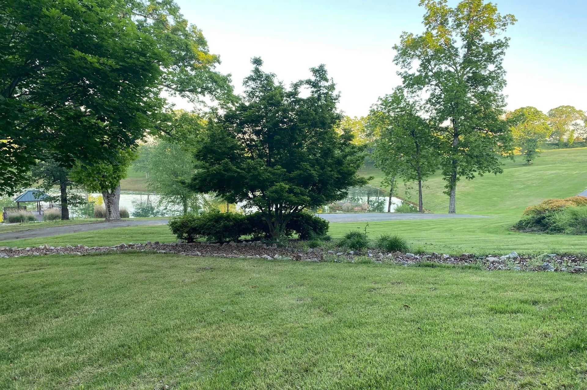 Green grassy yard with stone wall, trees, and lake in the background.