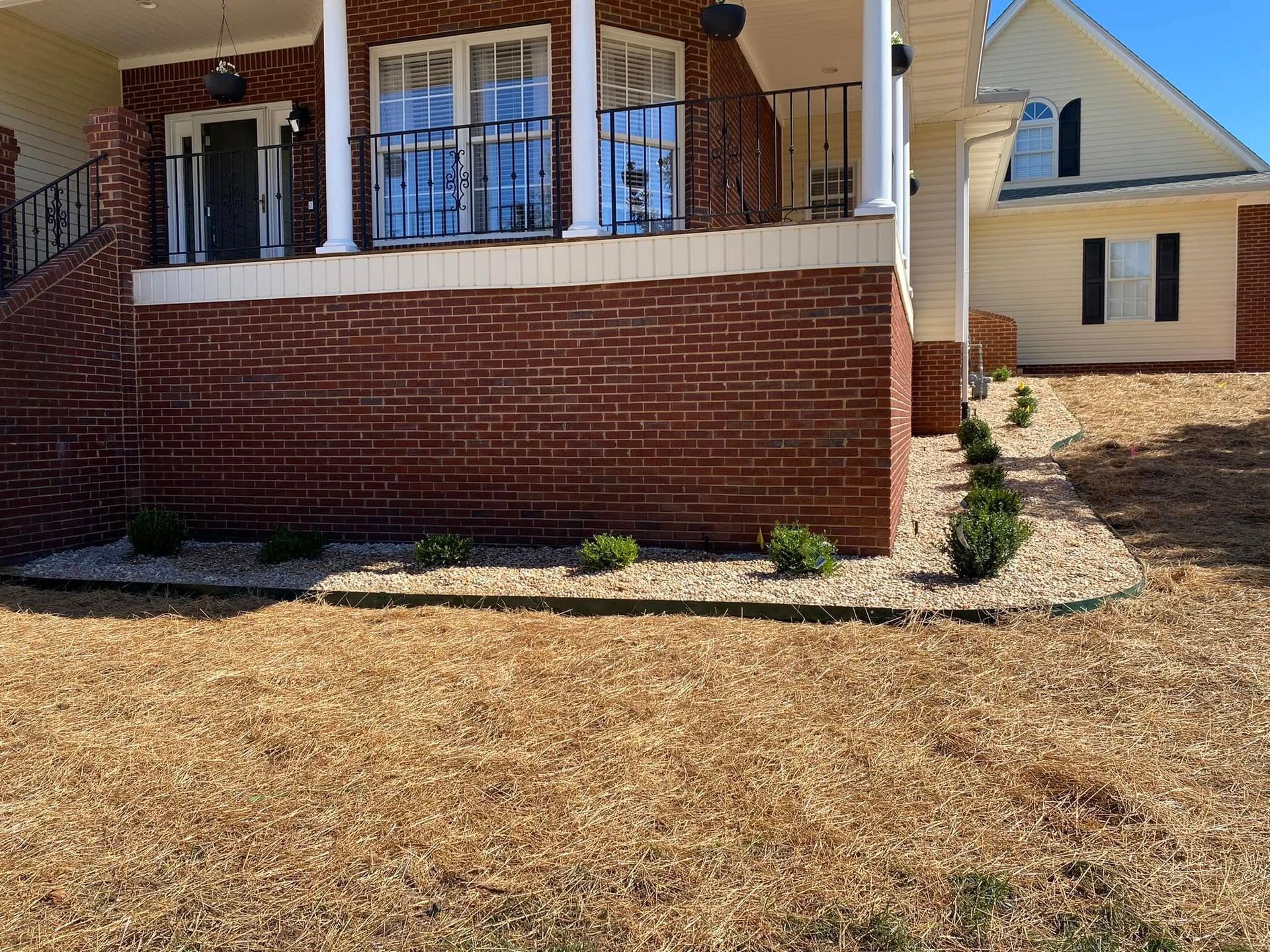 Front porch of a brick house with white railings and a dry, brown lawn in front.