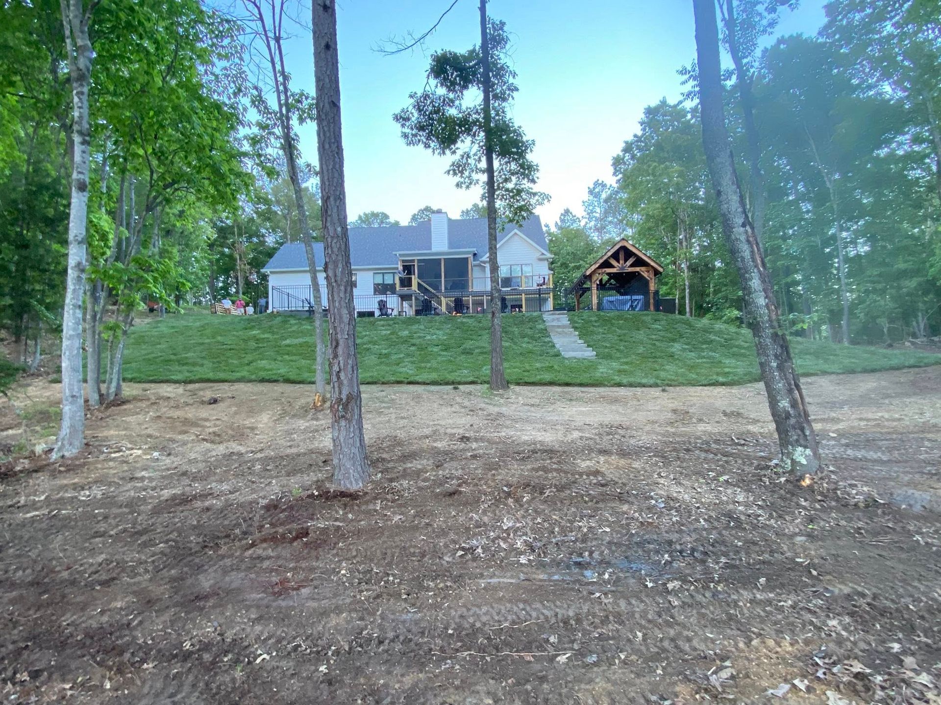 Leaf-covered yard beside a house, with a red excavator on the left and autumn trees in the background