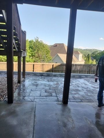 Covered patio with wet stone floor, wooden fence, and a view of houses and trees beyond.