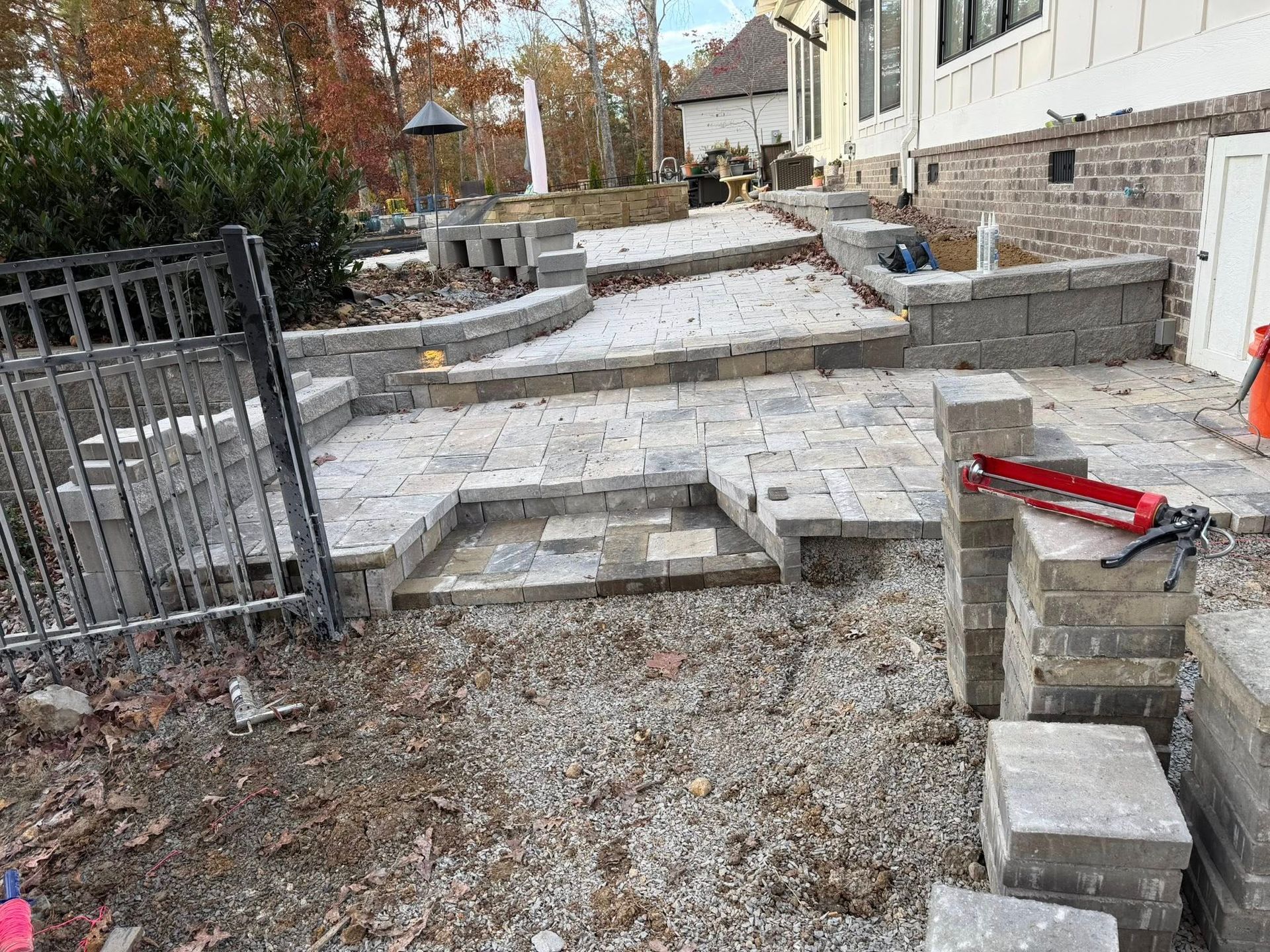 Partially built stone patio and steps beside a house, with gravel and construction materials around it
