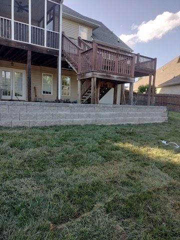 Backyard with raised wooden deck, concrete retaining wall, and grassy lawn under a partly cloudy sky