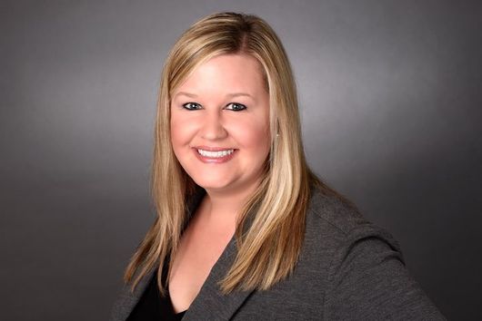 A woman in a gray jacket is smiling for the camera.