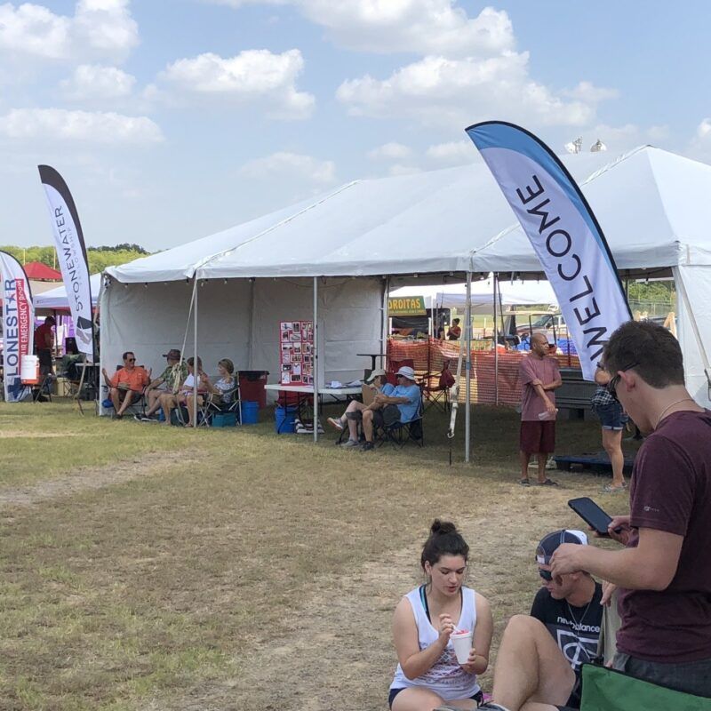 A group of people sitting under a tent with a welcome flag