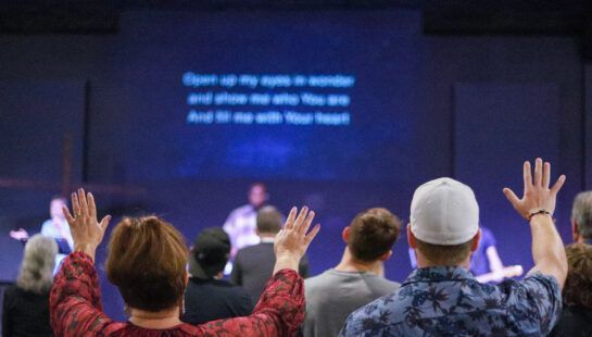 A group of people are raising their hands in the air in a church.