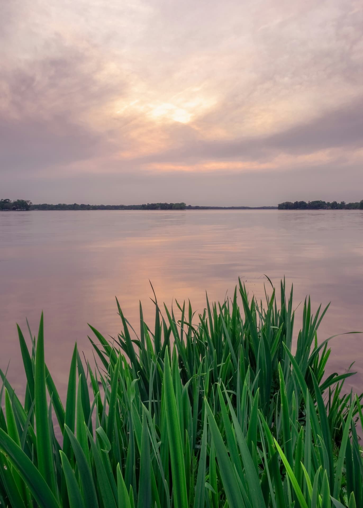 A wooden walkway leading to a gazebo overlooking a body of water at sunset.