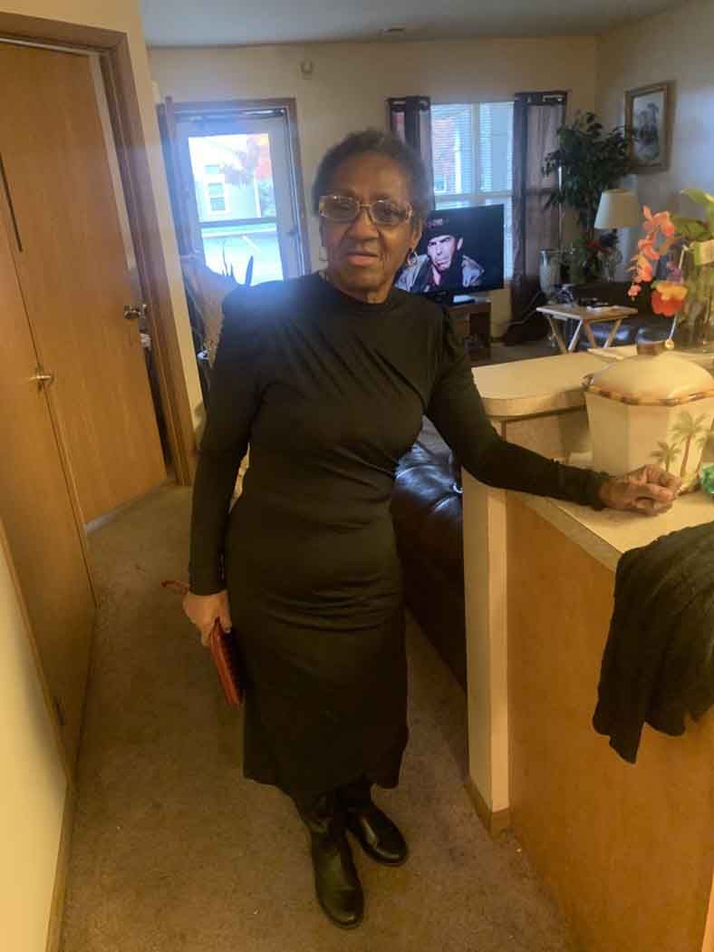 A woman in a black dress is standing in a living room.