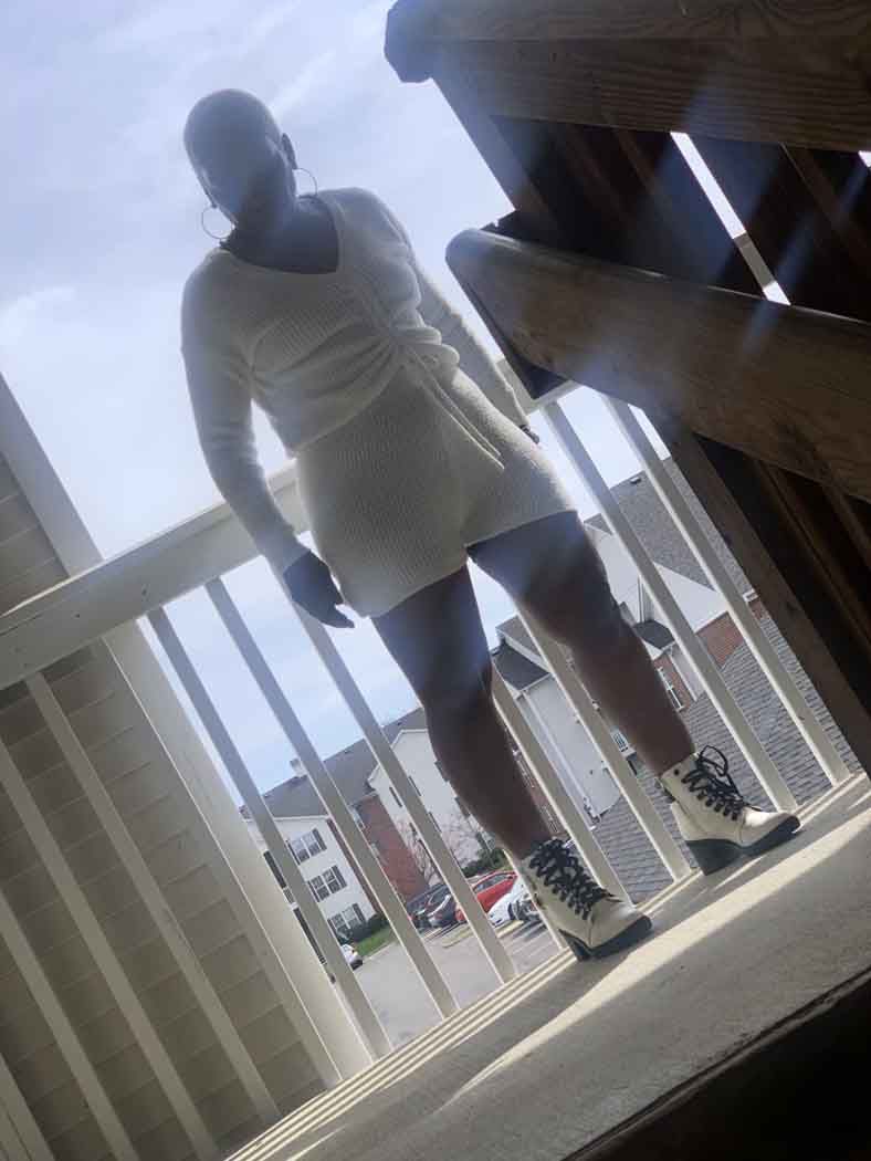 A woman in a white dress and white boots is standing on a balcony.