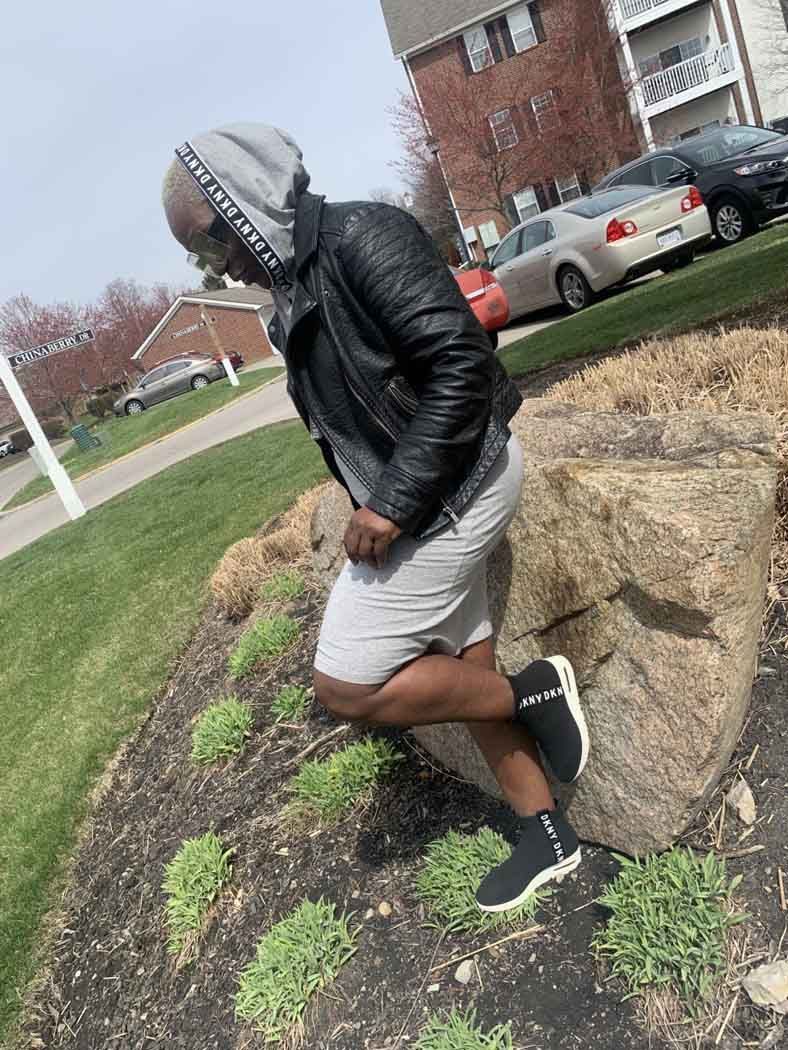 A man in a leather jacket and shorts is kneeling on a rock.