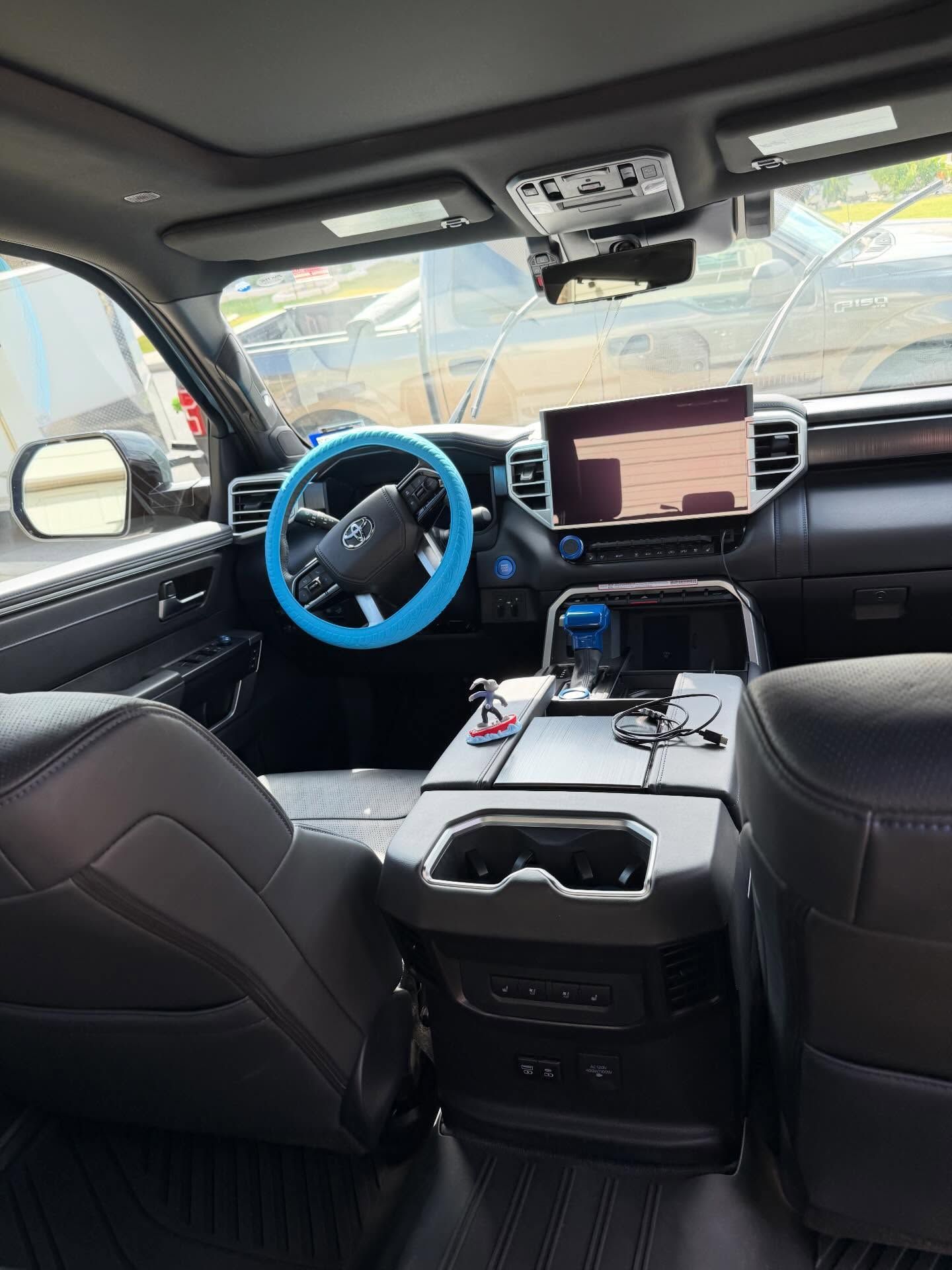Car interior with blue steering wheel cover, center touchscreen, and devices on the center console