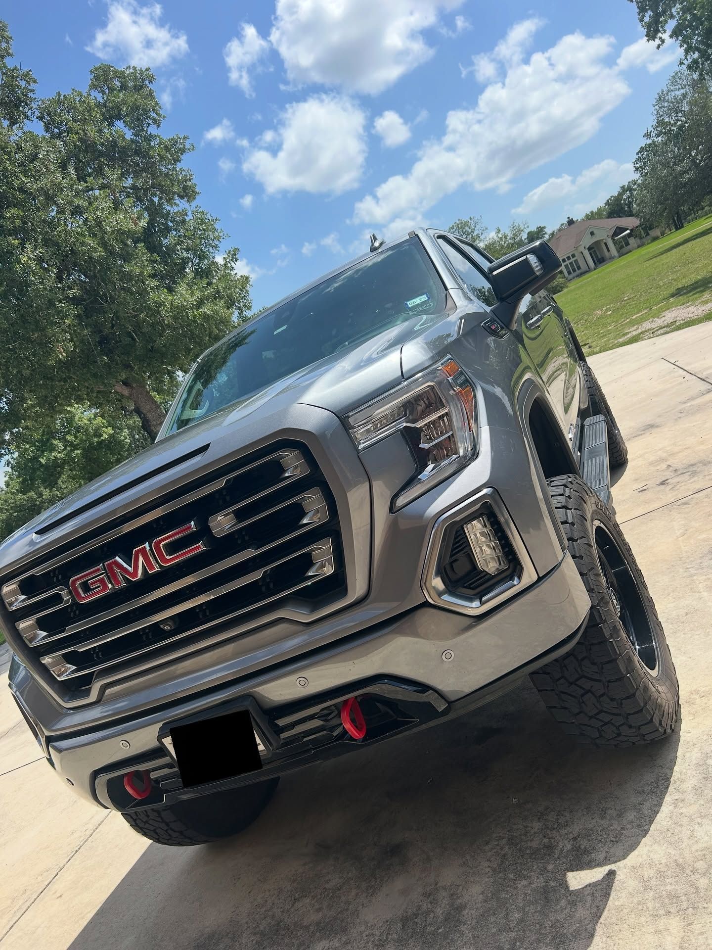 Silver GMC SUV angled in a driveway on a sunny day, with trees and blue sky in the background