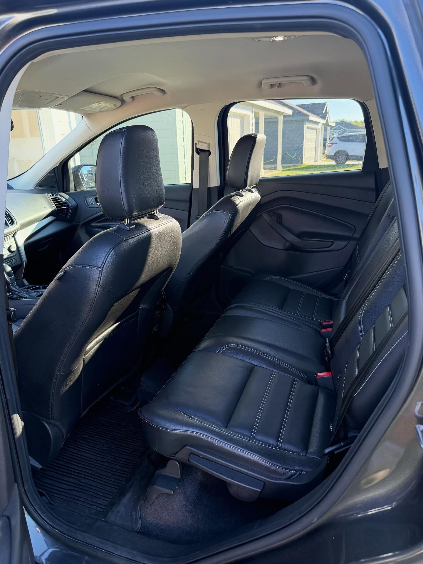 Rear view of a car’s black leather back seat with the door open, showing the interior from outside.