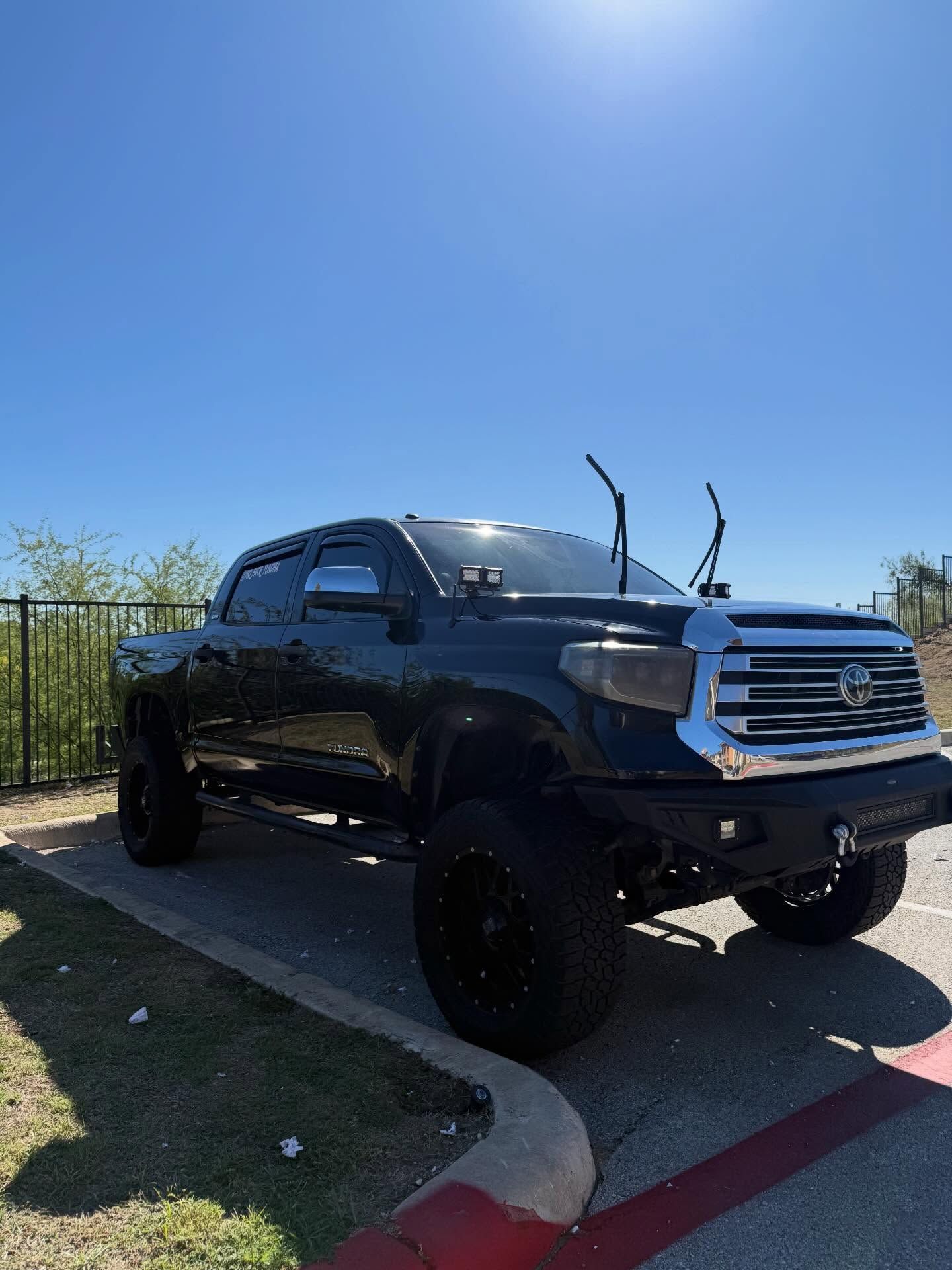 Black lifted pickup truck parked by a curb under a bright blue sky