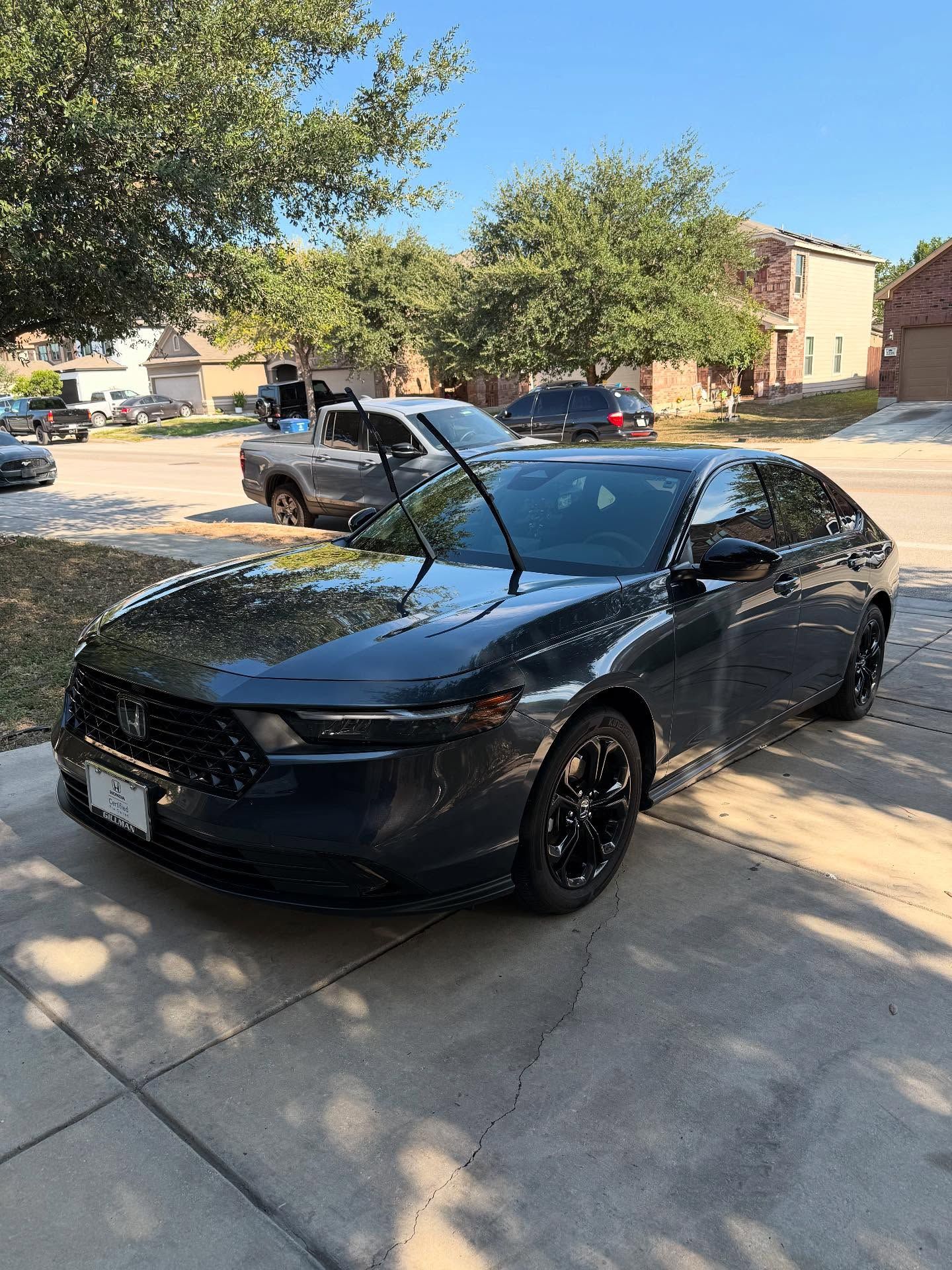 Black sedan with open hood parked in a sunny residential driveway