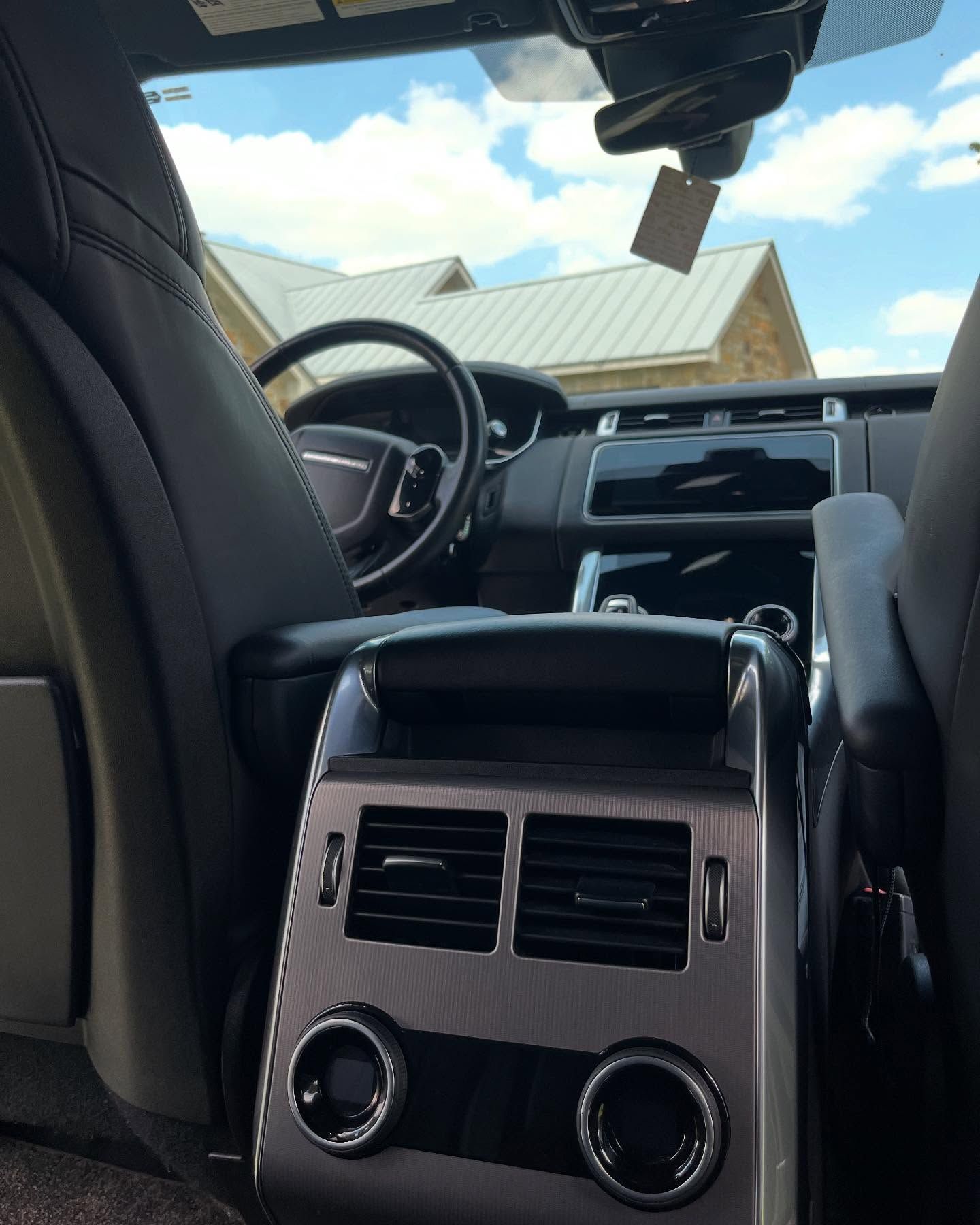 Backseat view of a car interior with steering wheel, dashboard, and sunroof under a bright sky