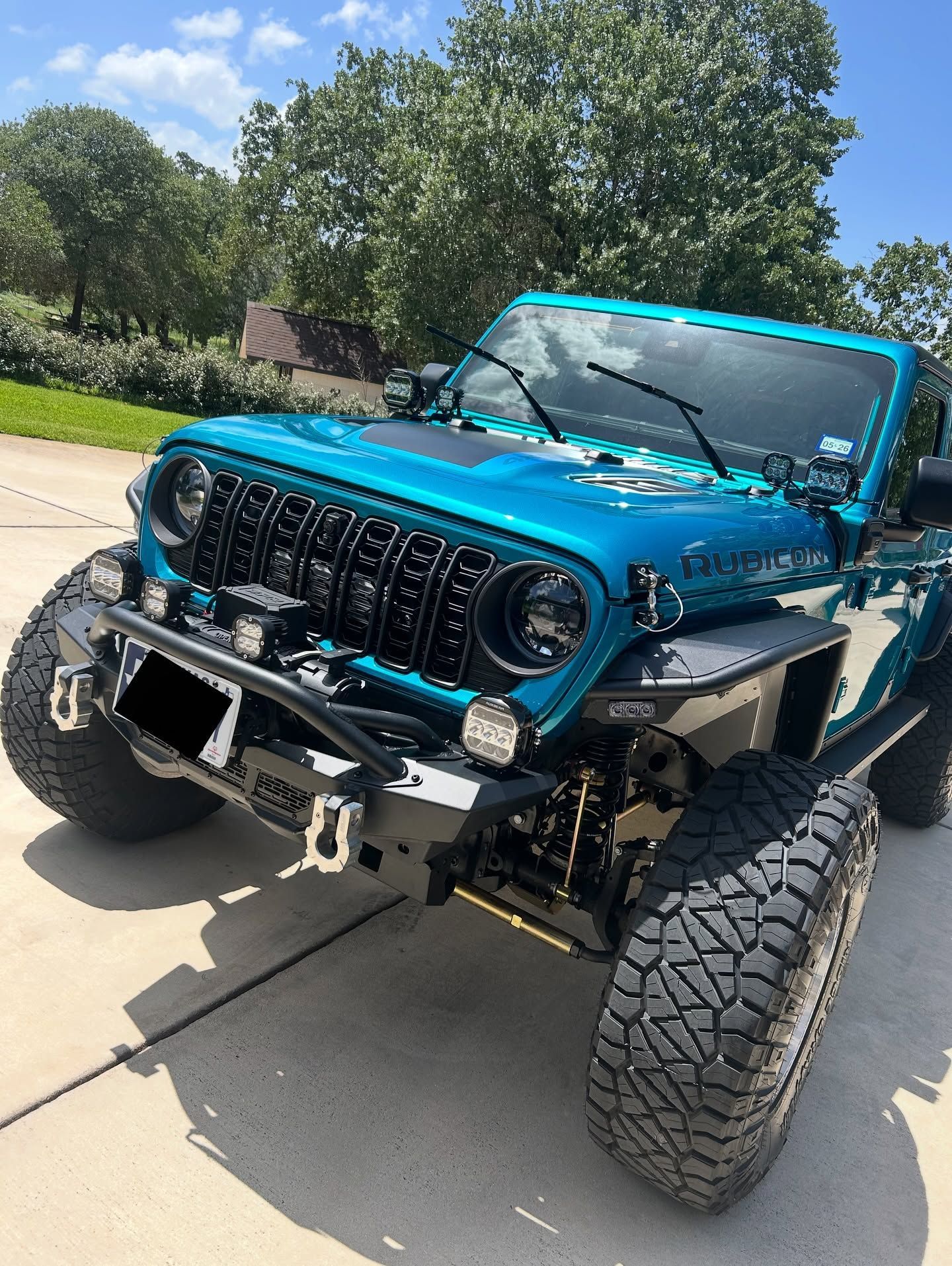 Blue off-road Jeep with lifted suspension and large tires parked on a driveway.