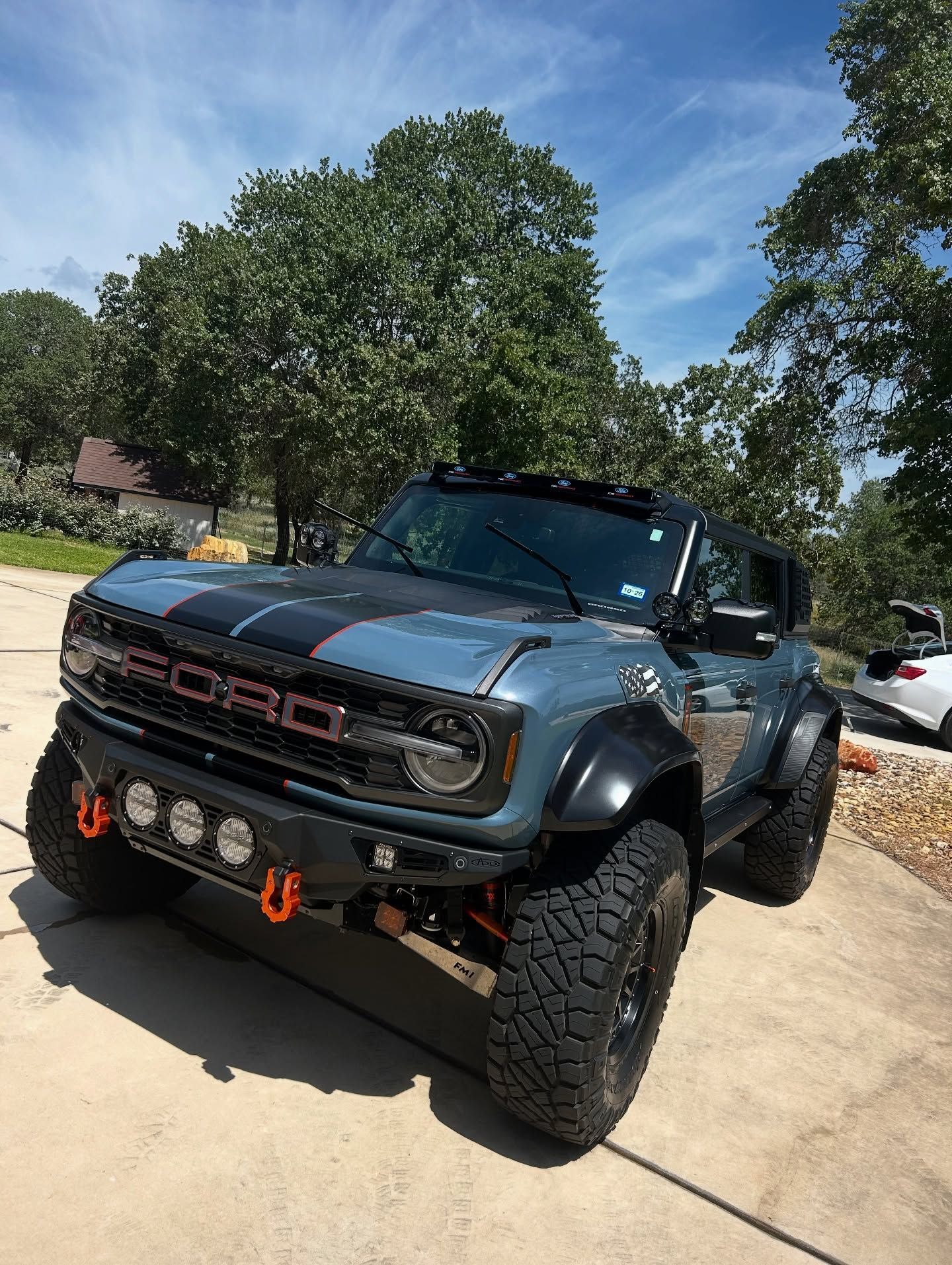 Blue off-road Ford Bronco parked in a driveway, with lifted suspension and a sunny suburban background.