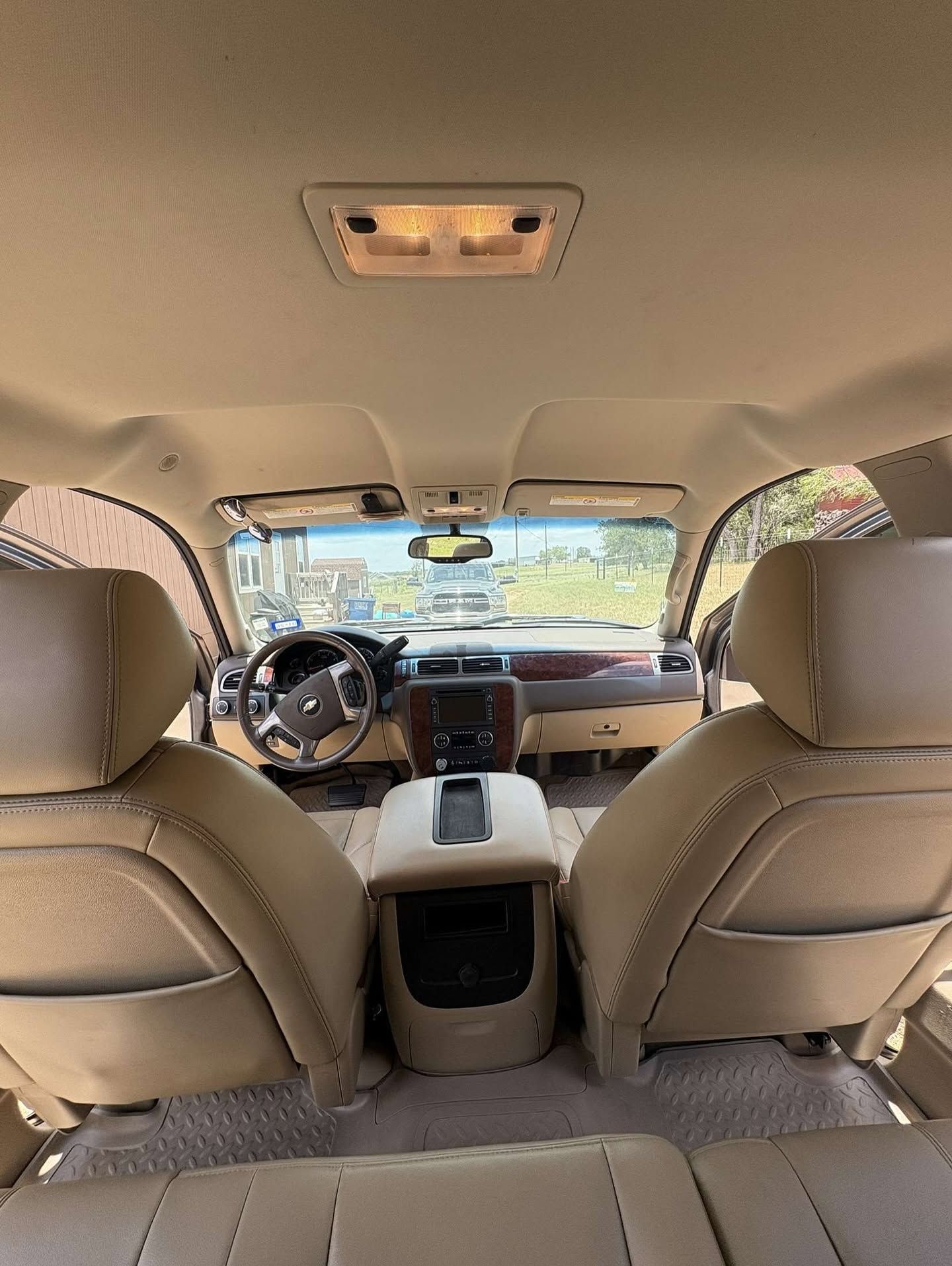 Car interior from the back seat, showing beige seats, center console, and windshield view of a street.