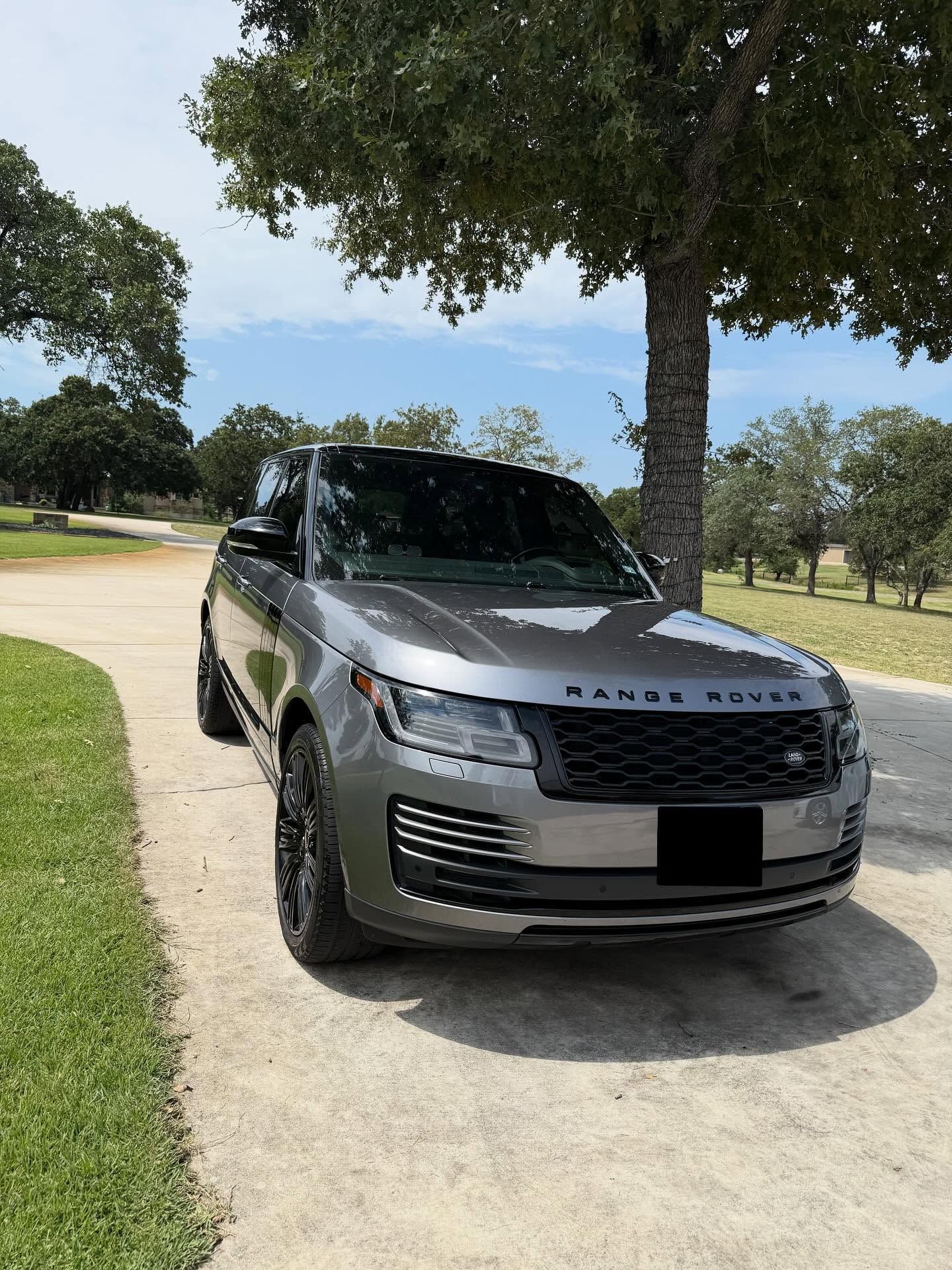 Silver Range Rover parked on a sunny roadside beneath a tree, with grass and blue sky in the background