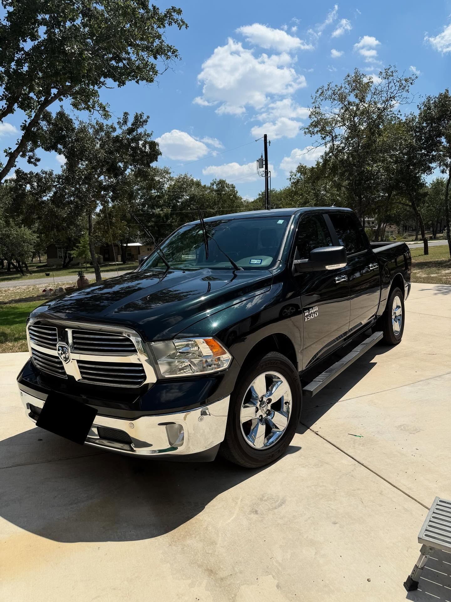Black Dodge Ram pickup truck parked on a sunny driveway near trees and blue sky