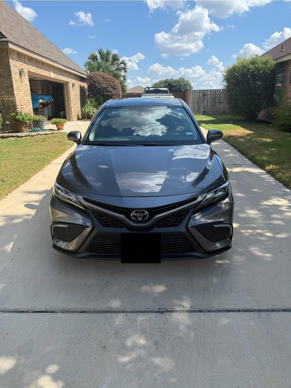 Black sedan parked in a suburban driveway under a sunny sky, front view.