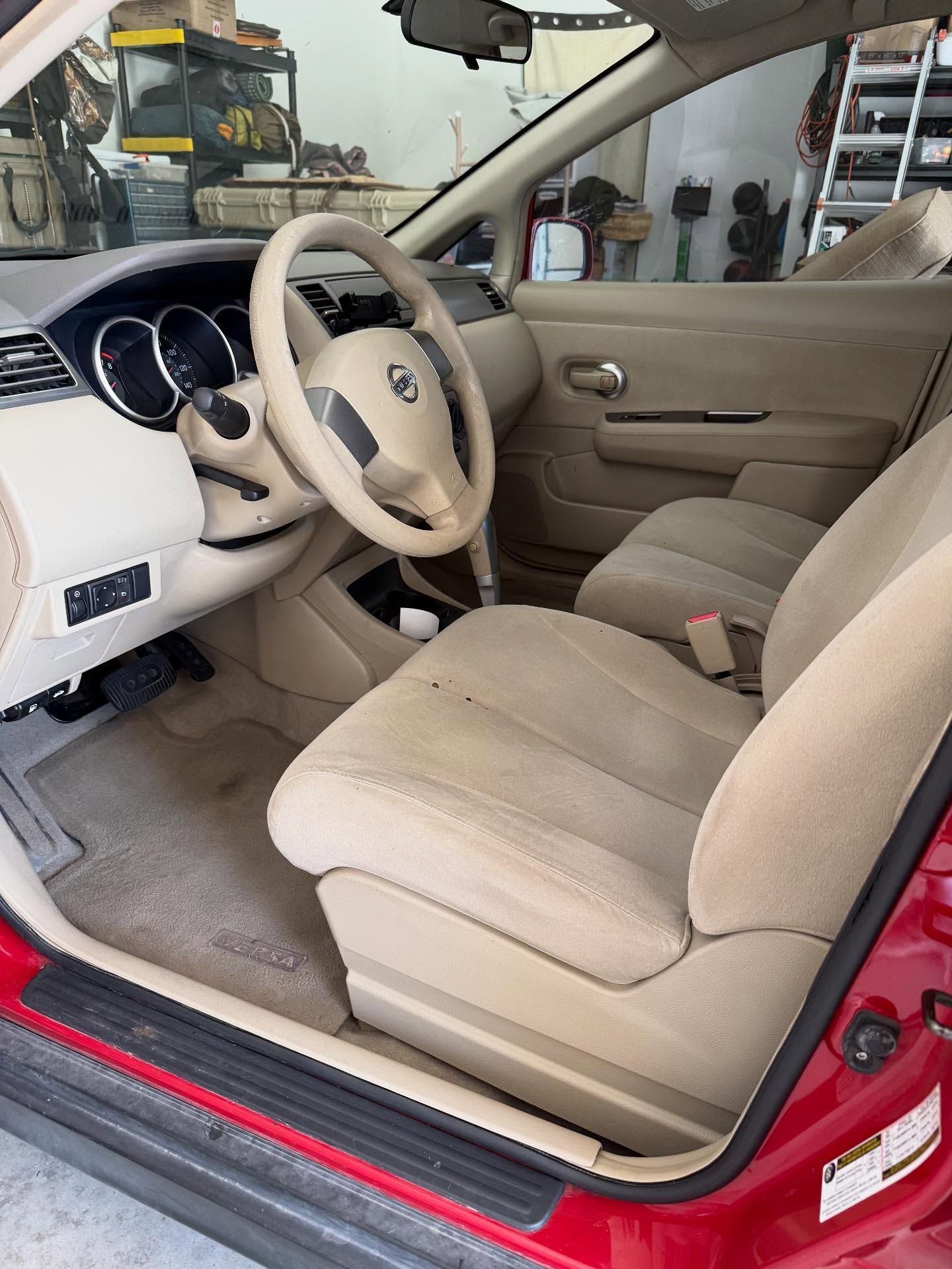 Beige car interior with open red door, front seats, and steering wheel visible.